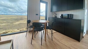 Una cocina moderna con armarios oscuros, un microondas y un lavamanos. Hay una mesa redonda de madera con cuatro sillas, y un ventanal con vistas a un paisaje cubierto de césped.