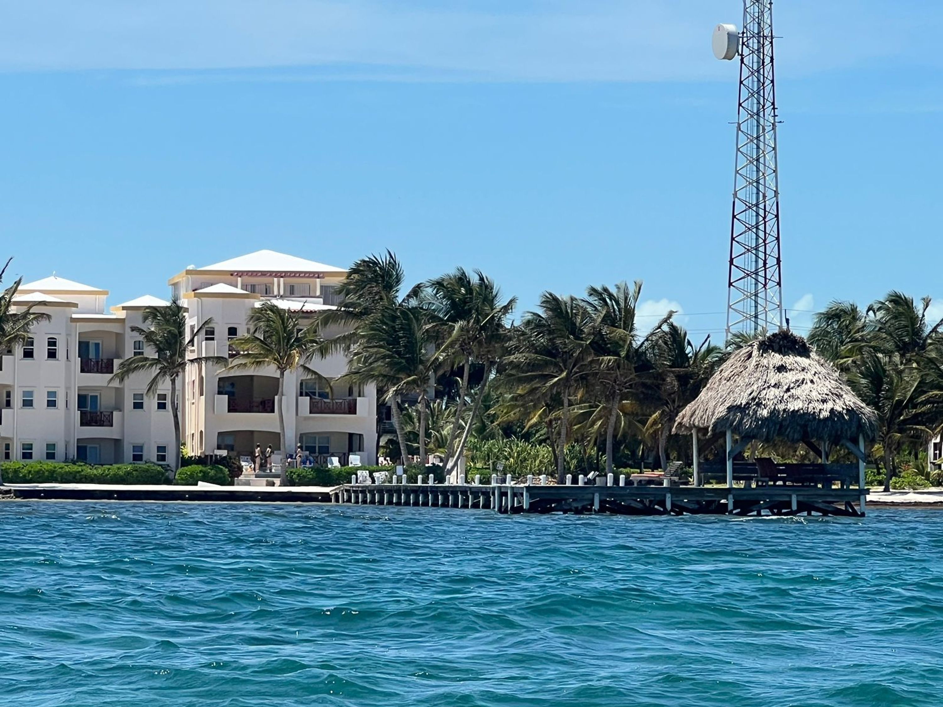 A coastal hotel with multiple balconies, a thatched-roof structure, and a pier extending into the water.