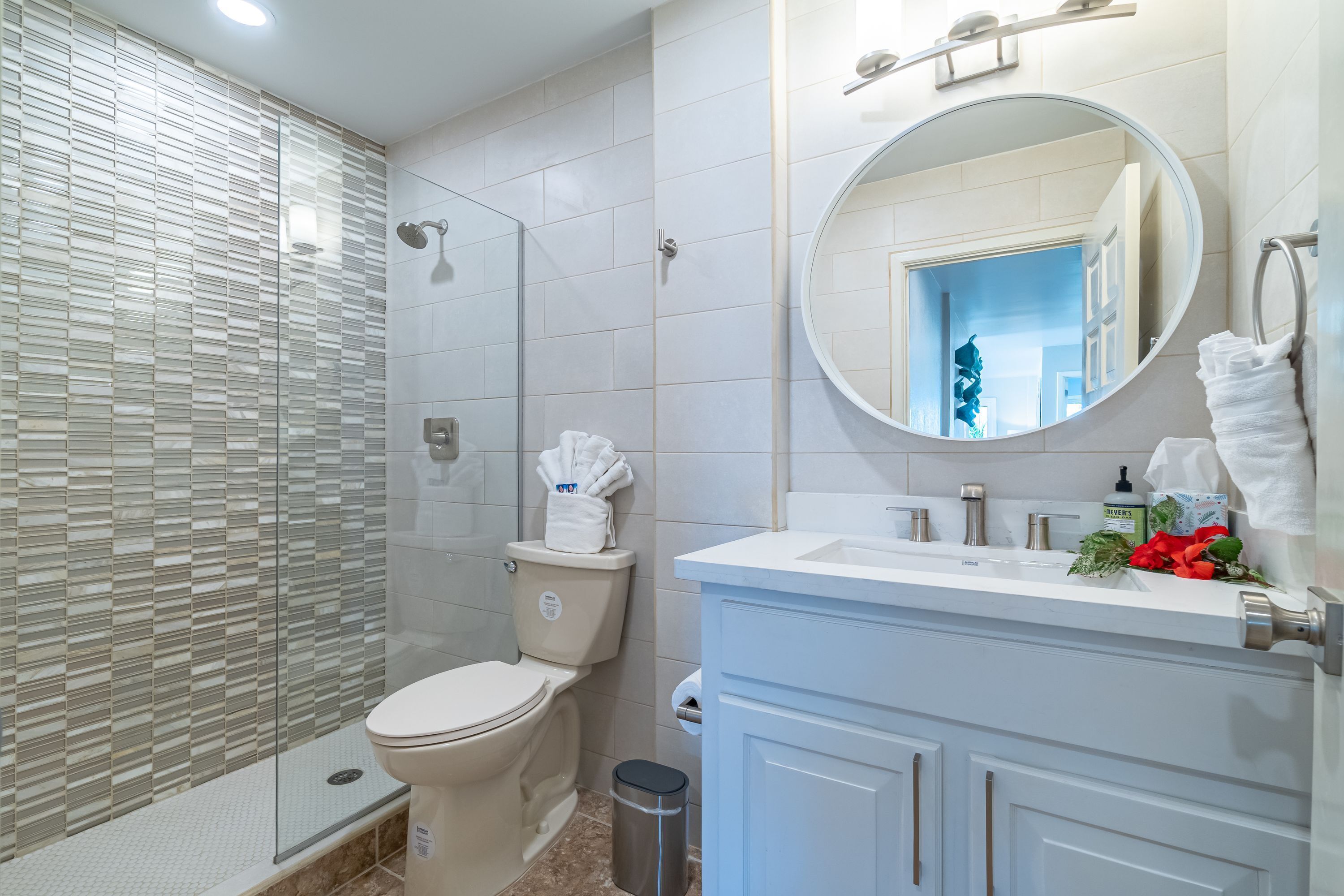 A modern bathroom with a glass shower enclosure, a toilet, a sink with a mirror, and a trash can.