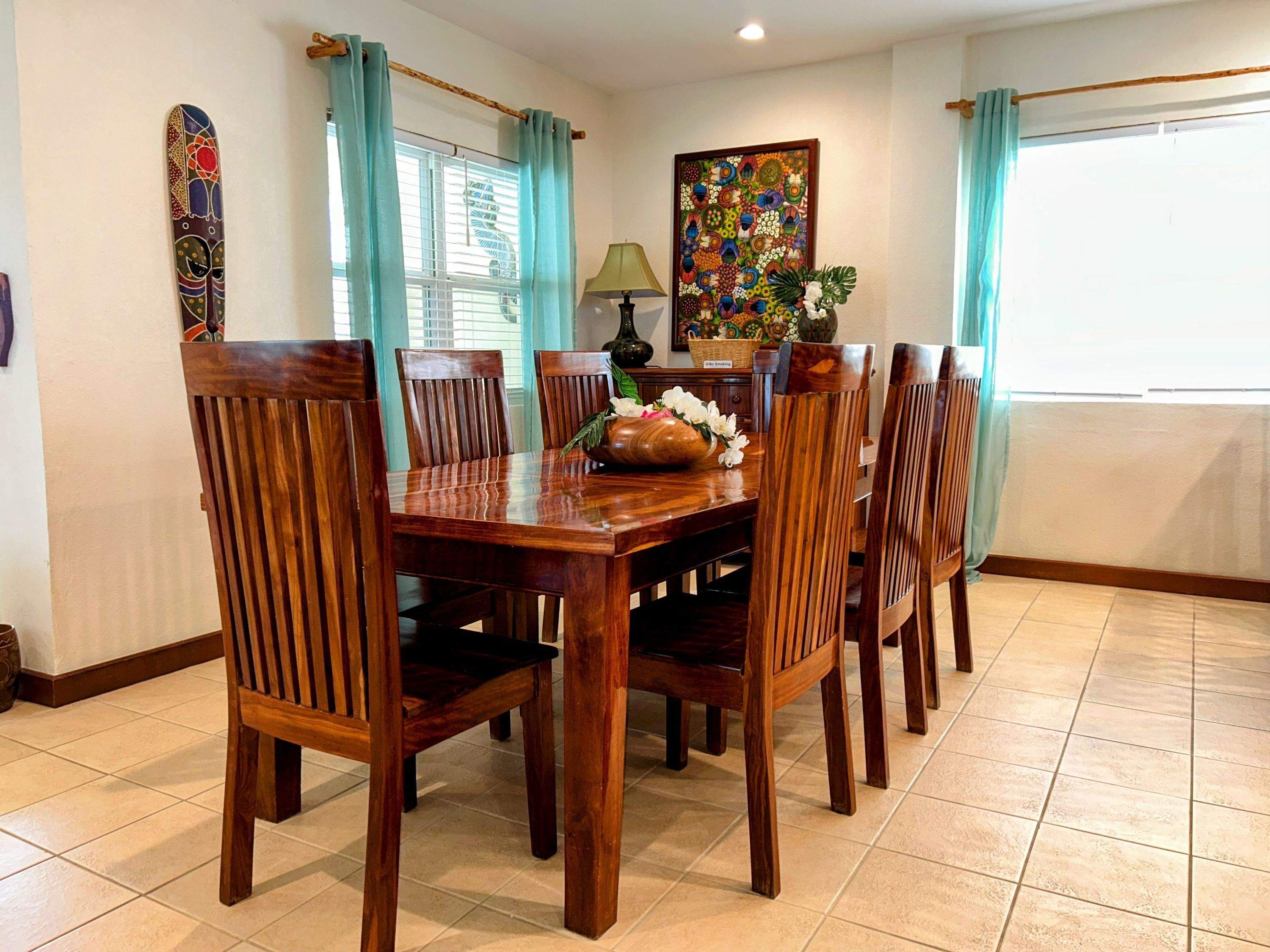 Un coin repas avec une table et des chaises en bois, un vase rempli de fleurs et un tableau coloré accroché au mur.