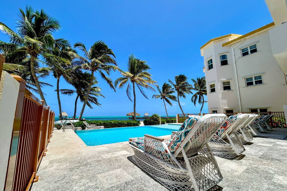 A poolside area with lounge chairs, a clear blue sky, and palm trees.