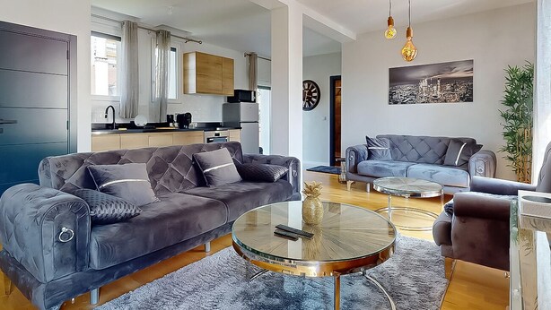 A modern living room with two sofas, a coffee table, and a dining area with a small table and chairs. A kitchen is visible in the background. - Apartment Grand Standing 🍀 (Épinay-sur-Seine)