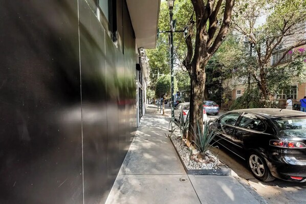 A sidewalk adjacent to a building with a parked car and trees.