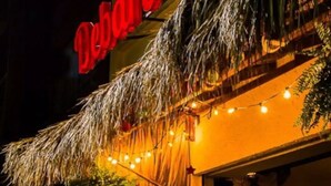 An outdoor seating area with tables and chairs, a thatched roof, string lights, and a building with a red sign. - Gorgeous studio with WiFi in Napoles (Napoles)