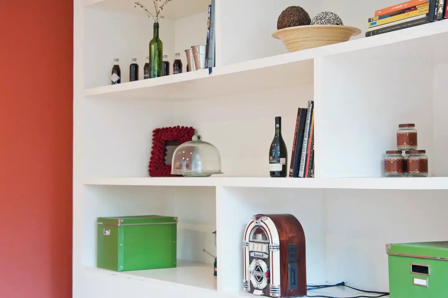 Ein Zimmer mit weißen Regalen, die verschiedene Gegenstände wie Bücher, Flaschen und dekorative Objekte zeigen.