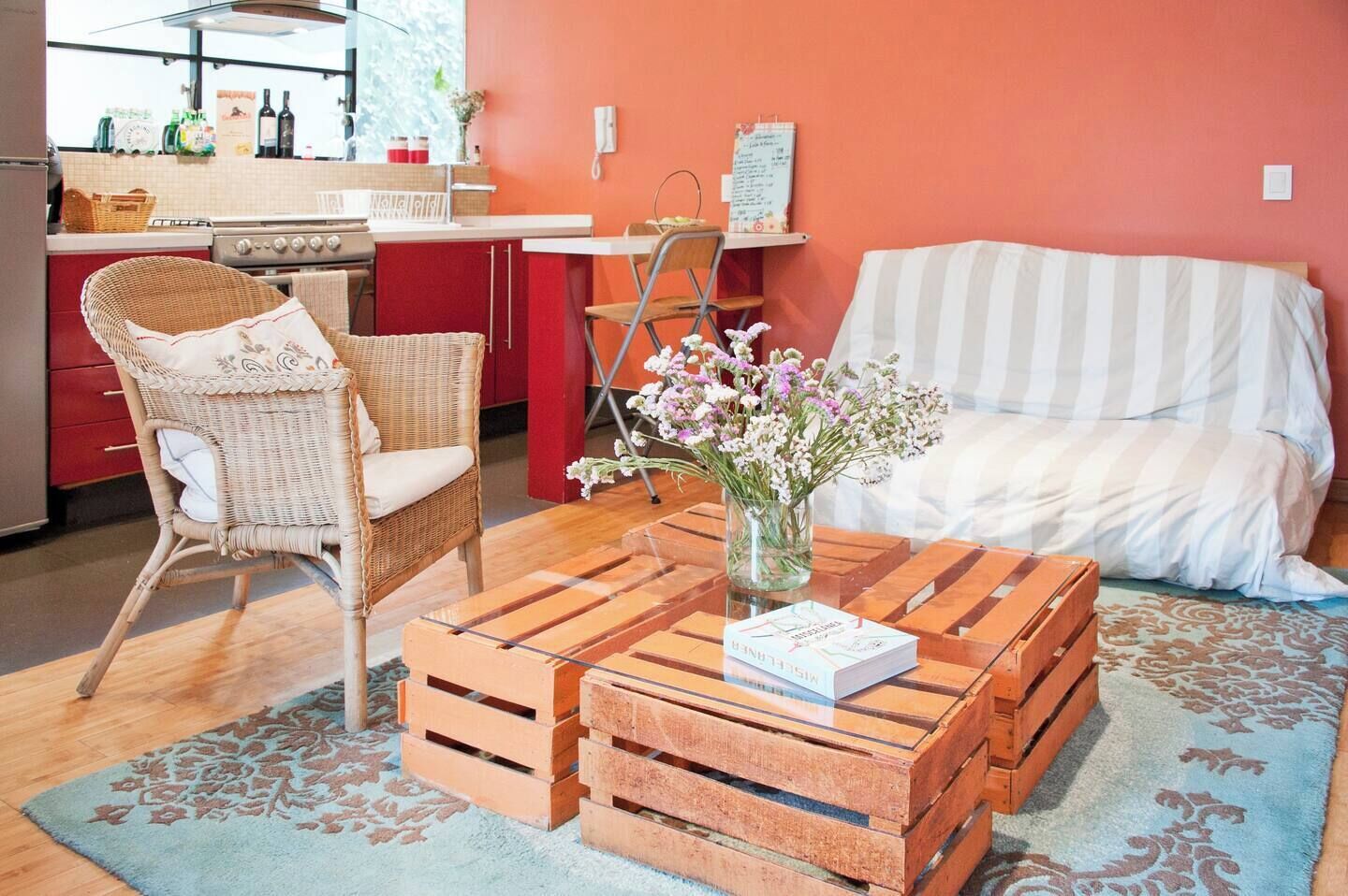 Ein gemütliches Wohnzimmer mit einem Korbstuhl, einem gestreiften Sofa und einem Couchtisch mit Buch und Blumen.