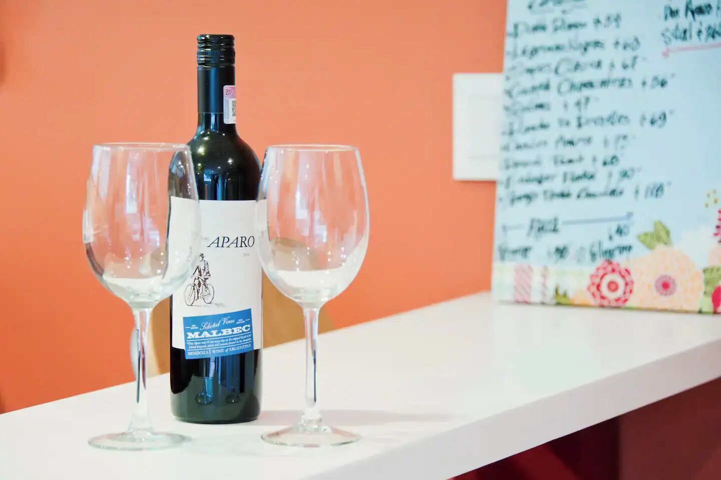 A bottle of wine and two glasses on a white table against an orange wall.