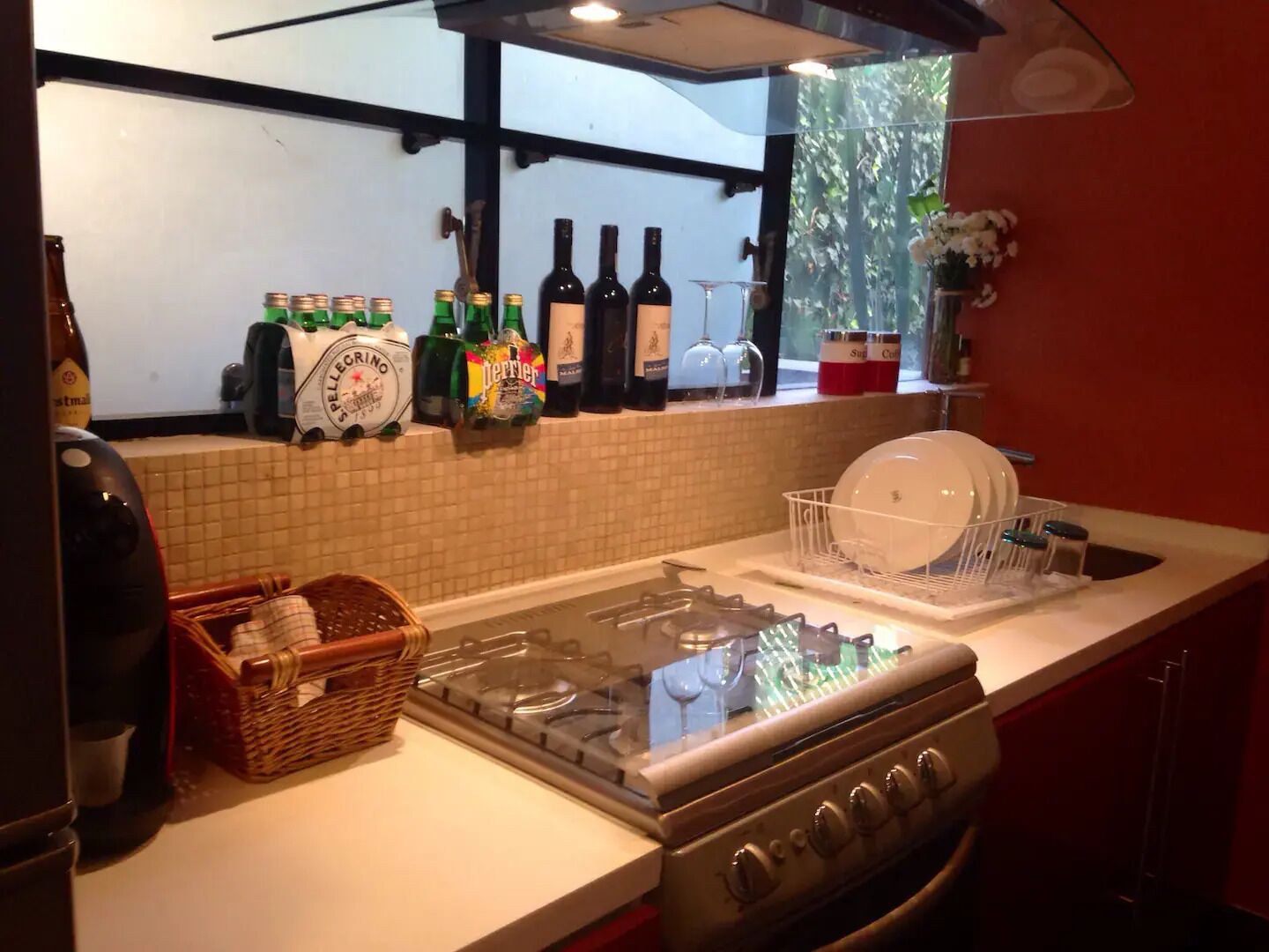 Una cocina con estufa a gas, escurreplatos y diversas botellas de cerveza y vino sobre la encimera.