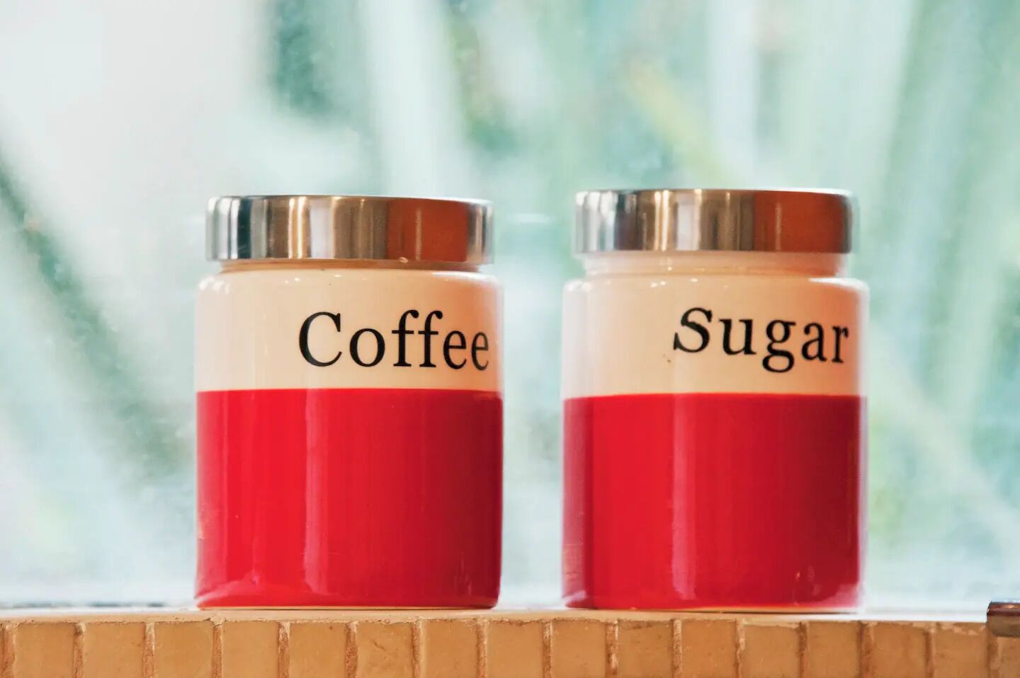 Deux bocaux étiquetés « Café » et « Sucre » sont posés sur une étagère.