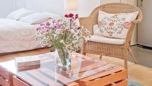 A bedroom with a bed, a wicker chair with a cushion, a glass coffee table with a vase of flowers, and a bedside table. - Gorgeous studio with WiFi in Napoles (Napoles)