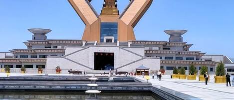 A modern building with a unique geometric structure, a central water feature, and a clear sky.