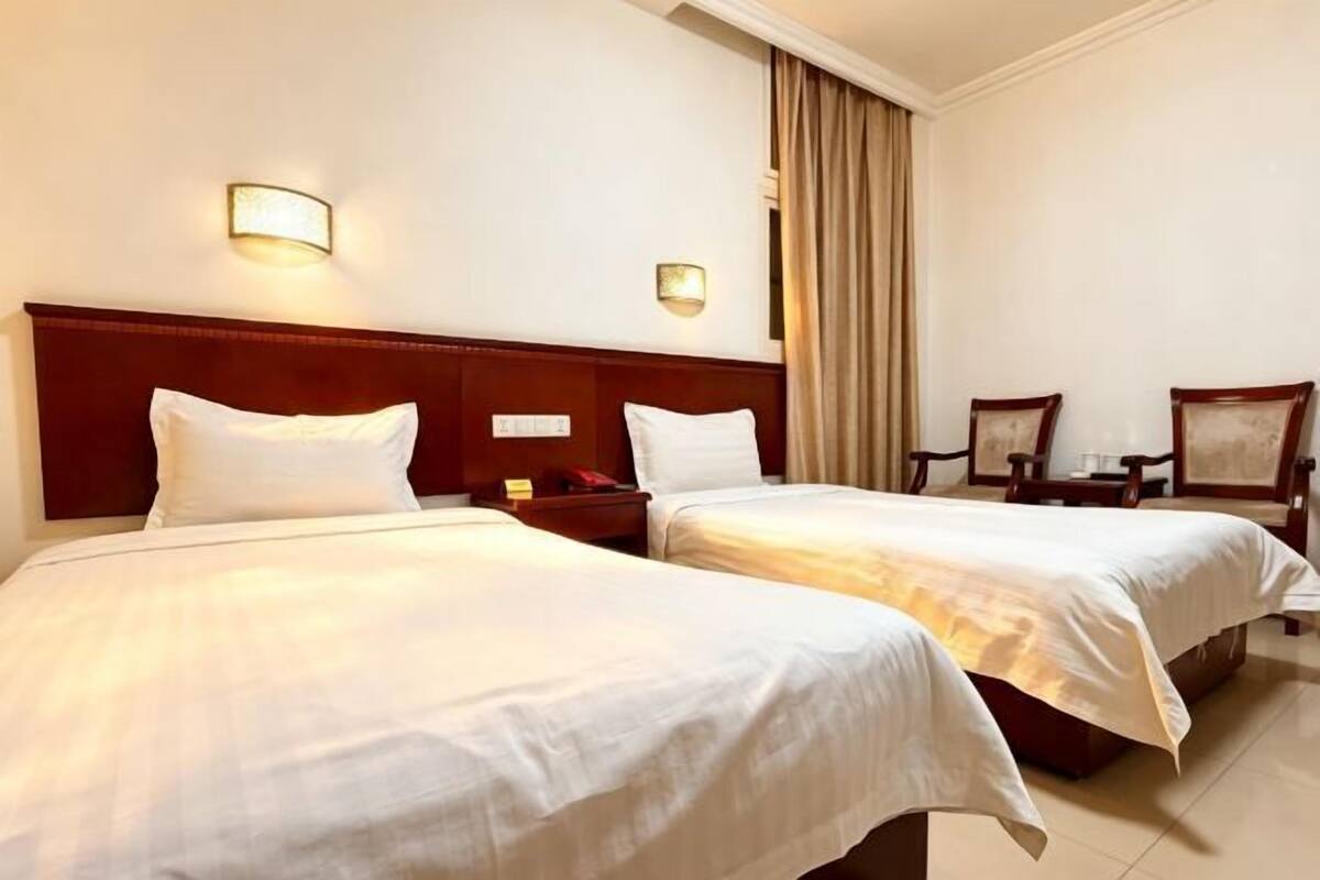 A hotel room with two beds, a nightstand, a lamp, and a chair.