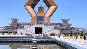 A modern building with a unique geometric structure, a central tower, and a reflective water feature in front. - Delong Hotel(Fufeng County Hospital Fufeng Bus Station Branch) (Fufeng County)
