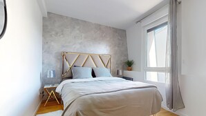Quarto moderno com cama, mesas de cabeceira, rodapé e janela com cortinas, além de uma parede com textura.