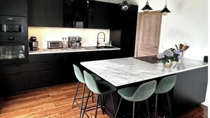 A modern kitchen with dark cabinetry, a marble island, and a wooden floor.