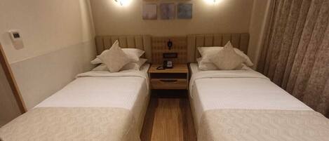 A hotel room with two beds, a wooden floor, a nightstand with a lamp, and wall-mounted artwork.