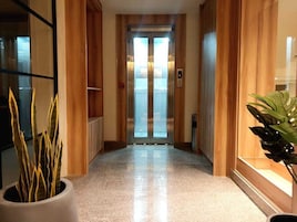 Un pasillo con suelo pulido, paneles de madera y puerta de vidrio para ascensor.
