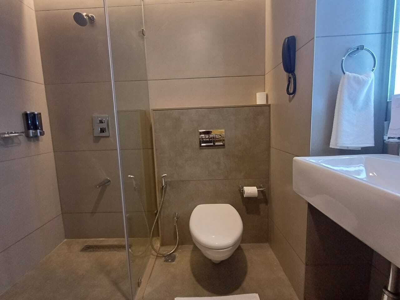 Egy modern fürőszoba üvegfalas zuhanyzóval, WC-vel és mosdókagylóval.