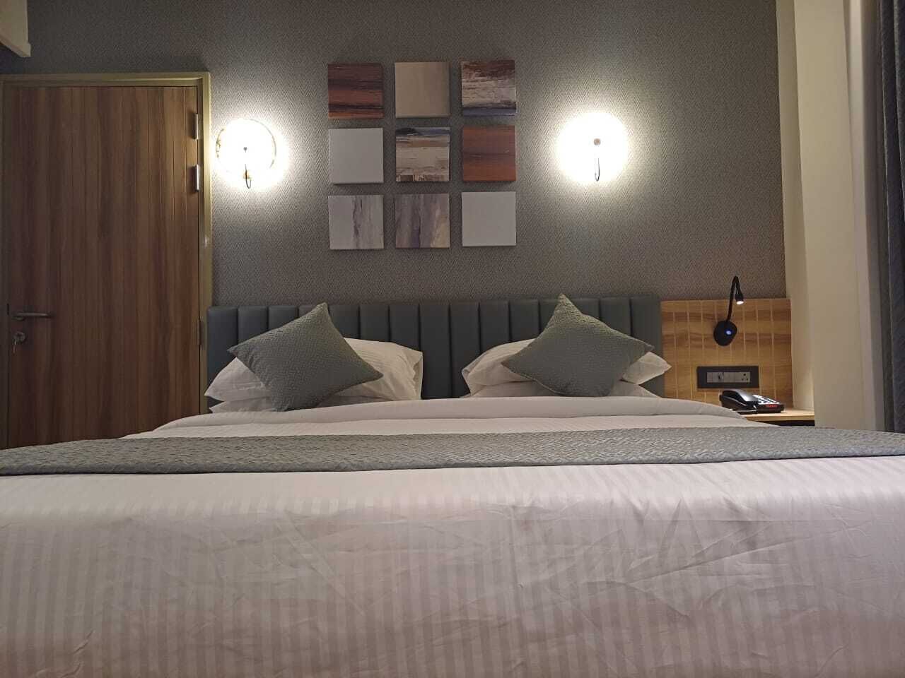 A neatly made bed with a grey headboard, two bedside lamps, and a wall-mounted clock.