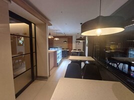 Un moderno comedor con mesas, sillas, una partición de vidrio e iluminación colgante.