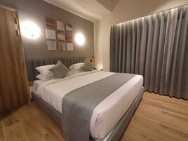 A modern bedroom with a large bed, wooden flooring, and a neutral color scheme.