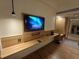 Una habitación de hotel moderna con una consola de madera, un televisor de pantalla plana montado que muestra una escena natural y un pequeño cubo de basura.
