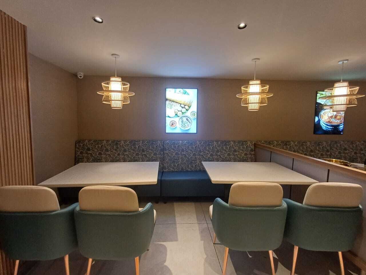 Un restaurante con una mesa larga, varias sillas, una pantalla de televisión e iluminación colgante.