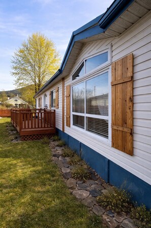 Une maison dotée d’une terrasse en bois, d’un chemin en pierre et d’une grande fenêtre avec des volets.