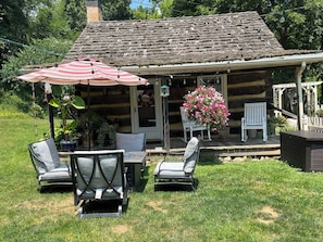 A rustic log cabin with a porch, outdoor seating, and a hanging flower pot. - Historic, cozy cabin at Headley Inn Winery & Vineyard with WiFi, AC & Fireplace (Zanesville)