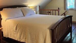 A bedroom with a wooden bed, white bedding, a wooden headboard, a window with curtains, and a ceiling vent. - Historic, cozy cabin at Headley Inn Winery & Vineyard with WiFi, AC & Fireplace (Zanesville)