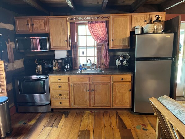 A kitchen with wooden cabinets, a stainless steel refrigerator, a sink, and a window with curtains. - Historic, cozy cabin at Headley Inn Winery & Vineyard with WiFi, AC & Fireplace (Zanesville)