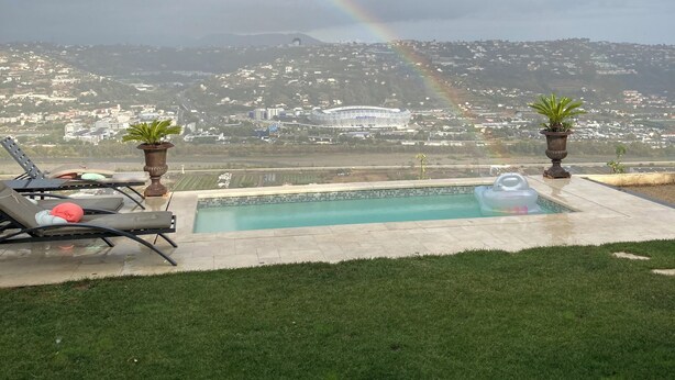 A pool with lounge chairs and potted plants, overlooking a cityscape and a rainbow. - A 15 mn de l Aèroport, Villa sur les Hauteurs de St Laurent du var (Saint-Laurent-du-Var)