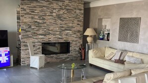 A modern living room with a stone wall, a flat-screen TV, a glass coffee table, and a beige sofa. - A 15 mn de l Aèroport, Villa sur les Hauteurs de St Laurent du var (Saint-Laurent-du-Var)