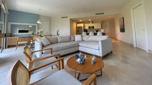 A modern living room with a sectional sofa, wooden chairs, a coffee table, and a ceiling fan. - Exotic Getaway 2BR in Plaza Puntarena (Rio Hato)