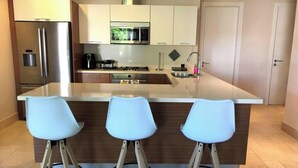 A modern kitchen with a central island, stainless steel appliances, and three bar stools. - Exotic Getaway 2BR in Plaza Puntarena (Rio Hato)