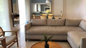 A living room with a beige sofa, a wooden coffee table with a plant, and a dining area in the background. - Exotic Getaway 2BR in Plaza Puntarena (Rio Hato)