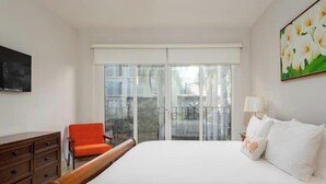 Een slaapkamer met een bed, een stoel, een dressoir, een televisie en een balkon met uitzicht.
