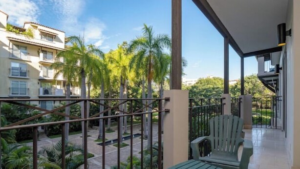 Een balkon met uitzicht op palmbomen en een gebouw op de achtergrond.
