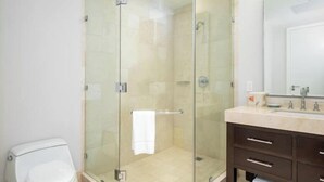 Een moderne badkamer met een douchecabine van glas, een wit toilet en een donker houten wastafelmeubel met spiegel.