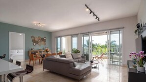Amplia sala de estar con sofá, mesa de comedor y sillas, ventanas grandes y un balcón con vistas.