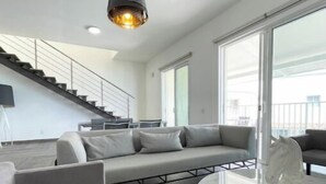 A modern living room with a grey sectional sofa, a glass coffee table, and a pendant light. - Family-Friendly 3BR Beachfront Puntarena (Rio Hato)