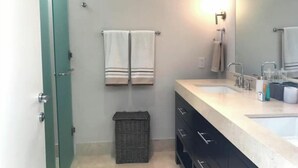 Ein Badezimmer mit einem großen Spiegel, zwei Handtüchern, die an der Wand hängen, einem Waschbecken und einem Mülleimer.