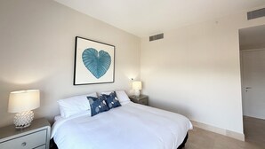 A bedroom with a bed, two bedside tables with lamps, a wall-mounted picture, and a door. - Tropical Retreat 2BR in Plaza Puntarena (Rio Hato)