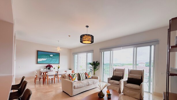 A spacious living room with a large window, a dining area, and a sofa with decorative pillows. - Tropical Retreat 2BR in Plaza Puntarena (Rio Hato)