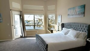 Een slaapkamer met een groot bed, uitzicht op een jachthaven en een schilderij aan de muur.