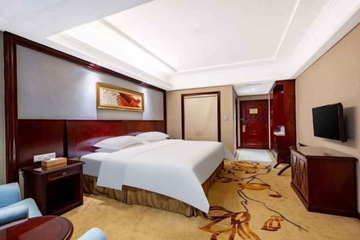 A hotel room with a bed, a desk, a chair, a television, and a painting on the wall.