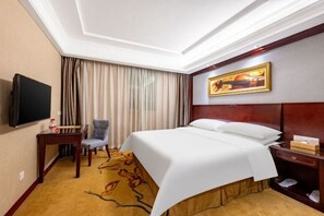 Una habitación de hotel con una cama, televisor, escritorio, silla y un cuadro en la pared.