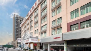 Et hotel med flere etager, moderne facade, flere balkoner og en parkeringsplads foran.