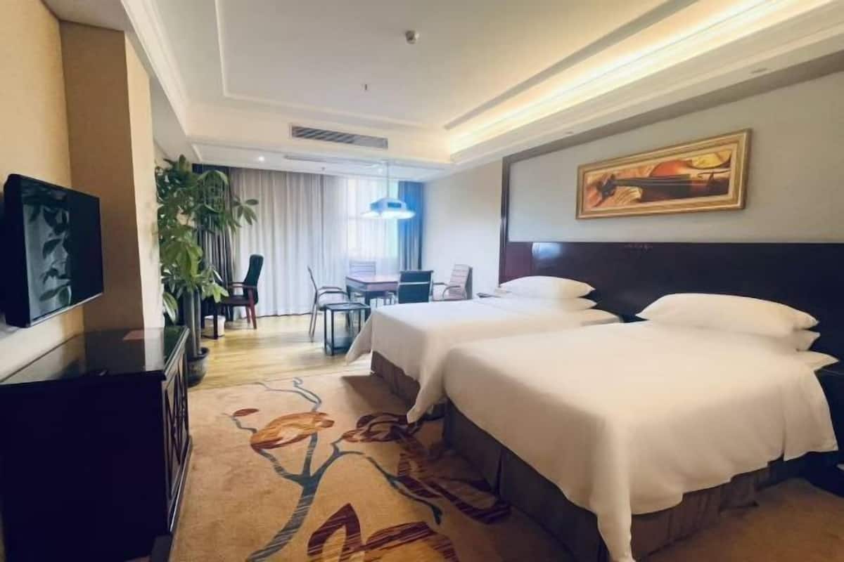 A hotel room with two beds, a desk, a chair, a television, and a large window.