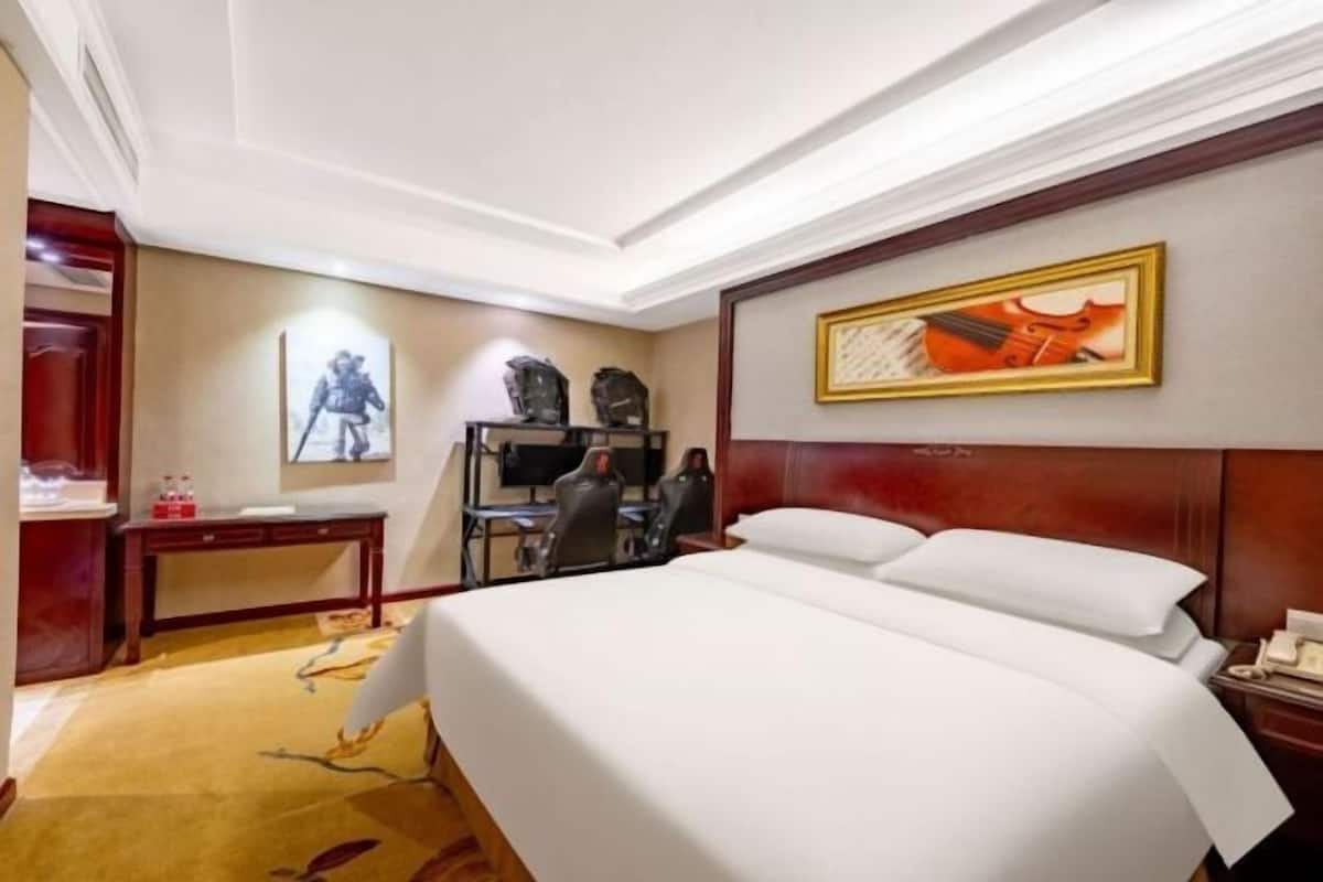 A hotel room with a large bed, a desk, a chair, and a TV.